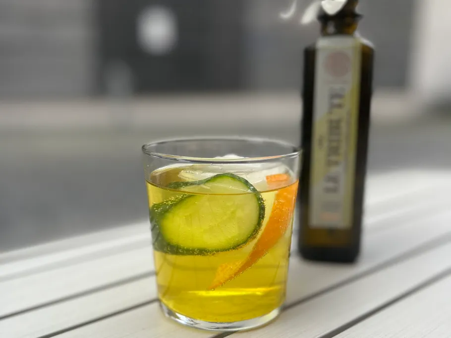 Glas mit Getränk, Gurke und Orange auf Tisch.