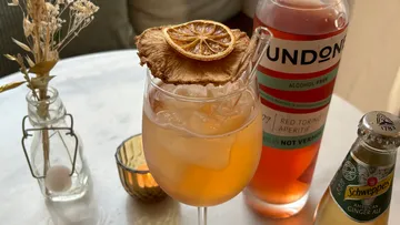 Cocktailglas auf Tisch mit Flaschen daneben.