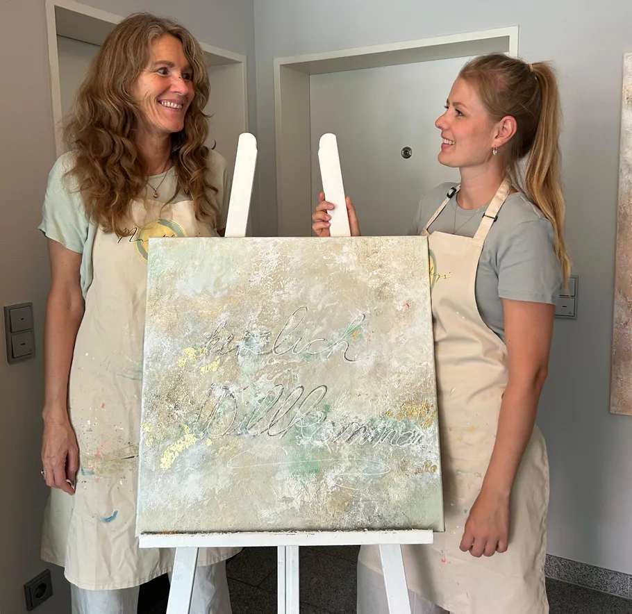 Two women smiling at an easel in a room.