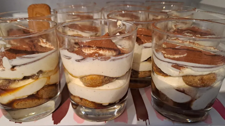 Tiramisu portions in glass cups on a table.