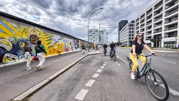 Cyclists riding beside graffiti-covered Berlin Wall.