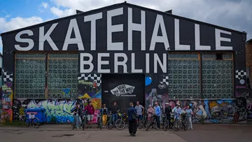 Personen mit Fahrrädern vor Graffiti-überzogenem Gebäude.
