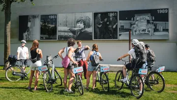 Cyclists listen to a guide outside historical photo exhibit.