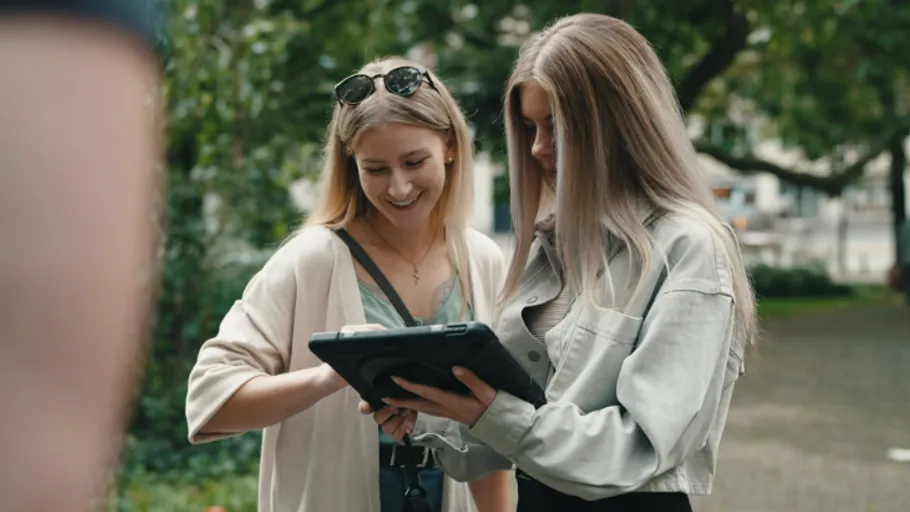 Zwei Frauen schauen draußen auf ein Tablet.