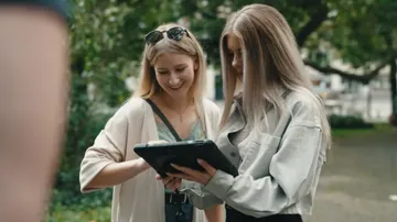 Zwei Frauen betrachten ein Tablet im Freien.