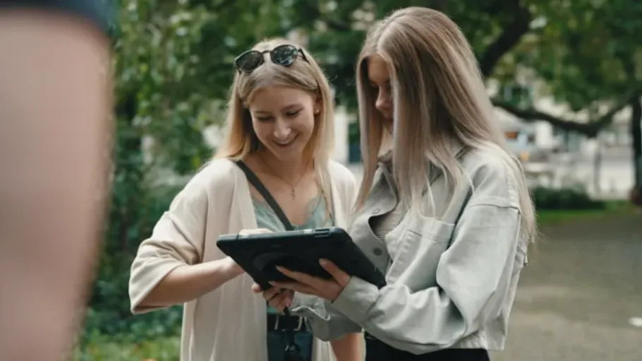 Zwei Frauen betrachten ein Tablet im Freien.
