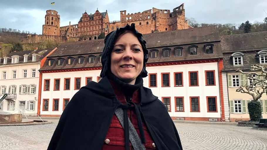 Person lächelt vor Schloss stehend.