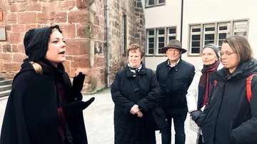 Person speaking to a group outdoors near buildings.