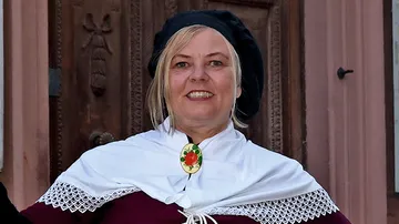Woman smiling, wearing traditional costume, wooden door background.