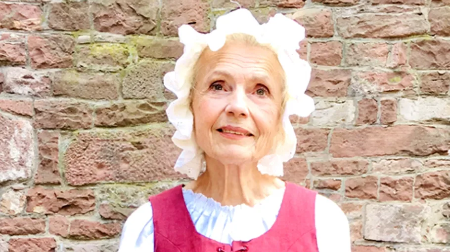 Woman in colonial attire poses against a brick wall.