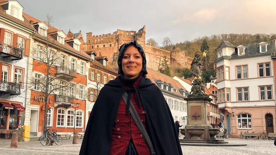 Person in cloak, historic town square, castle background.