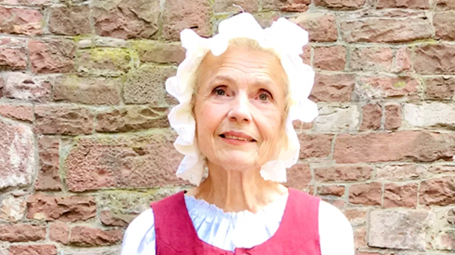 Elderly woman in bonnet, brick wall background.
