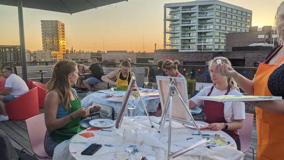 Group painting outdoors on a rooftop at sunset.