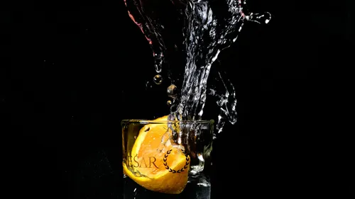 Lemon splashing into glass of water, dark background.
