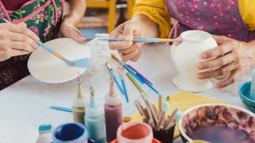 People painting pottery with brushes on table.