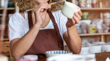 Person painting pottery in a studio environment.