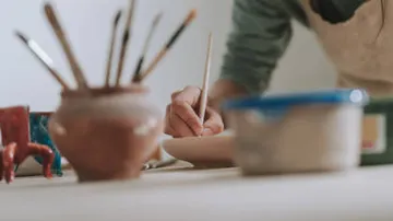 Person malt mit Pinseln auf einem Tisch.