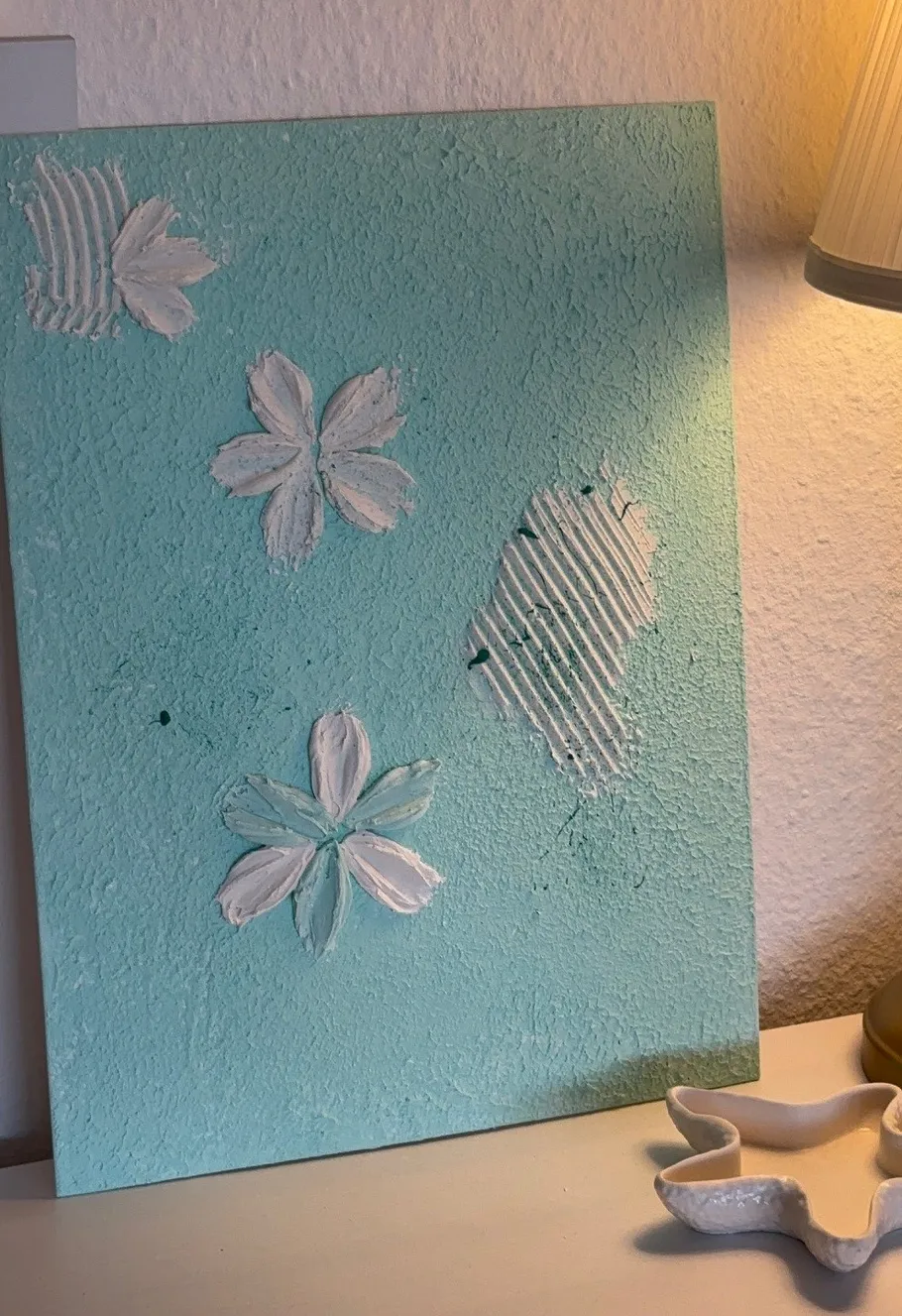 Strukturierte Kunst mit weißen Blumenmustern auf Türkis.