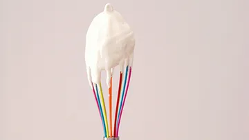 Schneebesen mit Sahne vor einfachem Hintergrund.
