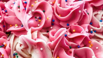 Nahaufnahme von rosa Zuckerguss mit bunten Streuseln.