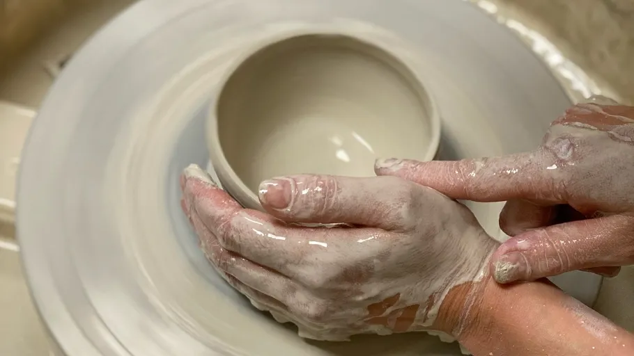 Hands shaping clay bowl on pottery wheel.