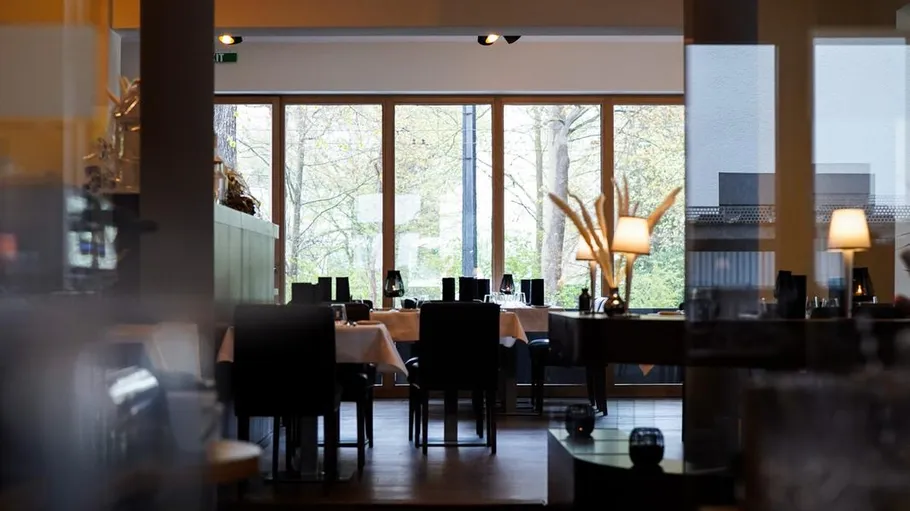 Leeres Restaurant mit Tischen und großen Fenstern.