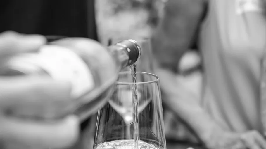 Weinflasche gießt Flüssigkeit in Glas, unscharfer Hintergrund.