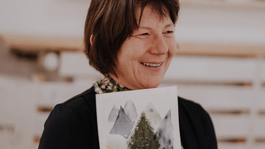 Woman smiling, holding a painting indoors.