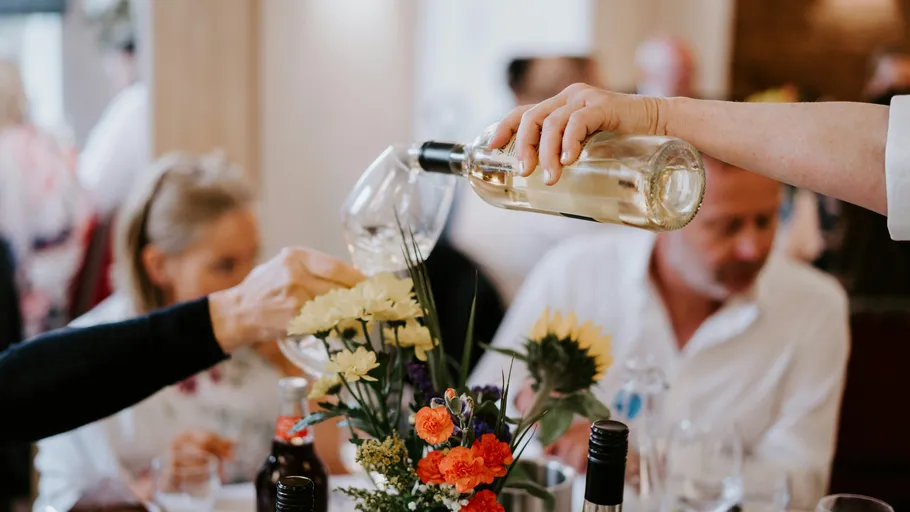 Person pours white wine at a table.