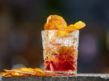Ein gläserner Cocktail mit Eis und Orangenstücken.