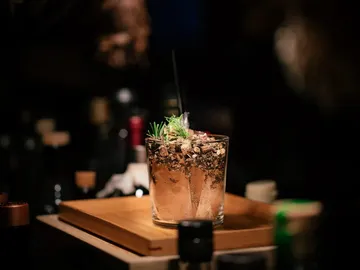 A cocktail is sitting on a wooden tray in a bar.