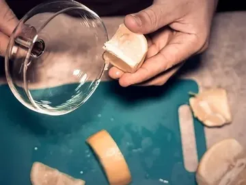 One hand holds a piece of cheese over a glass.