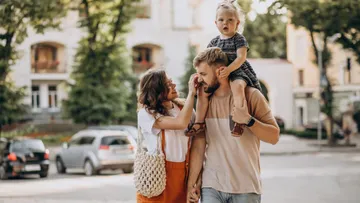 Family walking outdoors, child on father's shoulders.