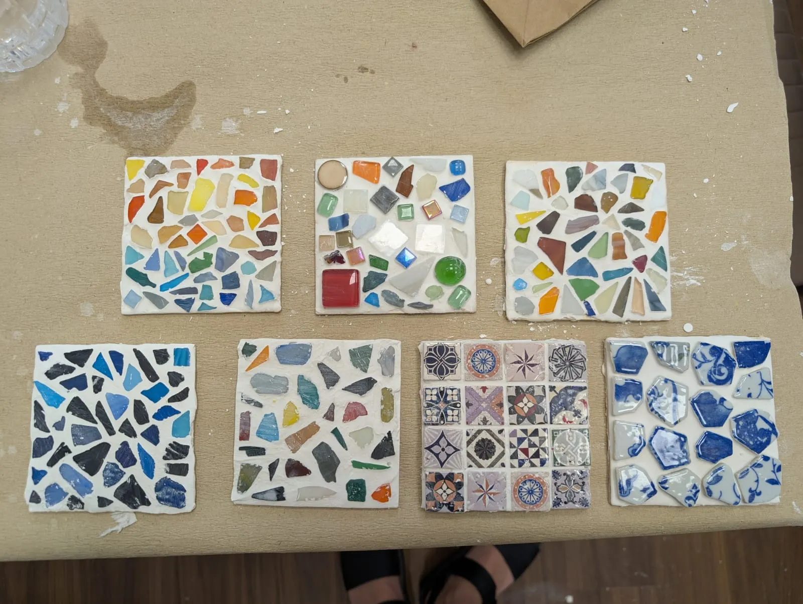 Sieben bunte Mosaikfliesen auf beiger Oberfläche.