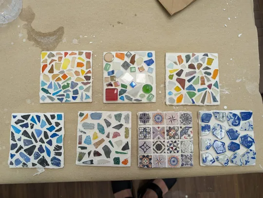 Sieben bunte Mosaikfliesen auf beiger Oberfläche.