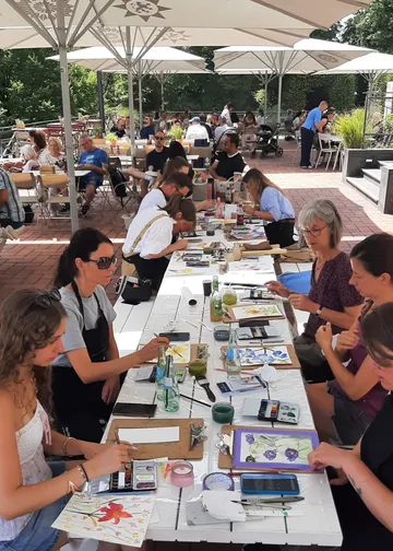 Group painting at outdoor cafe under umbrellas.