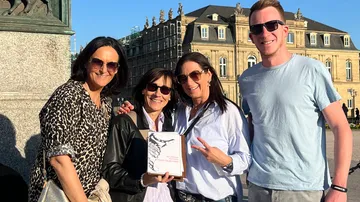 Four people posing with an award outside a building.