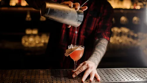 Barkeeper gießt Cocktail in schummrig beleuchteter Bar.