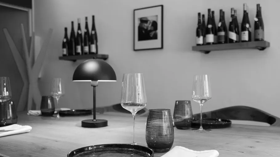 Dining table set with glasses, bottles on shelves.