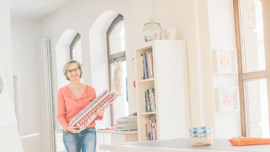 Woman holding fabric rolls in bright room.