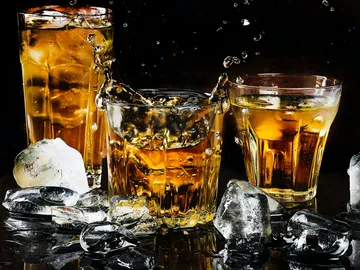 Drei Gläser mit Getränken spritzen Wasser in dunklem Umfeld.