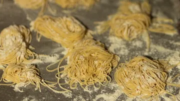 Fresh homemade pasta nests on floured surface.