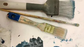 Three paintbrushes on a slightly painted surface.