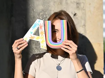 Frau hält bunte Buchstaben vor Gesicht.