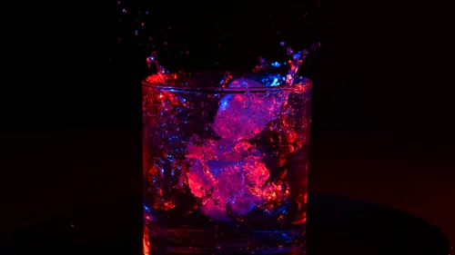 Glass with ice and splashes, red-blue lighting.