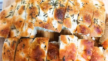 Sliced focaccia bread with herbs on board.