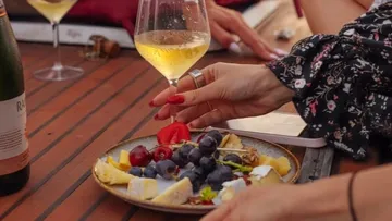 Hand holding wine glass near fruit plate.