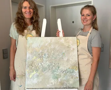 Two women holding a painted welcome sign.