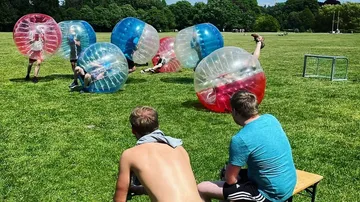People in inflatable bubbles playing on grass.