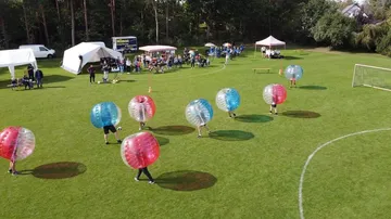 People playing bubble soccer on a grassy field.